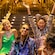 Four friends sit on a staircase as sparkling confetti falls around them