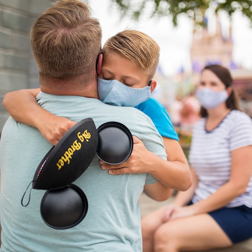 Un niño con orejas de Mickey bordadas con las palabras "Big Brother" abraza a un hombre