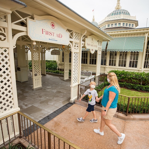 Una mujer y un niño con máscaras sostienen las manos mientras caminan a la estación de primeros auxilios en el parque Magic Kingdom