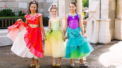 3 girls in princess dresses and fancy shoes pose in front of Cinderella Castle