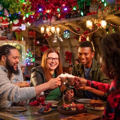 Un grupo de 4 amigos sentados en una mesa dentro de Jock Lindsey's Hangar Bar, levantando sus bebidas para hacer un brindis
