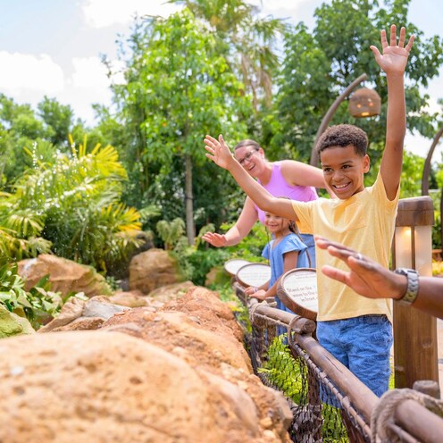 A family of 4 waves their hands to interact with a water feature on the Journey of Water, Inspired by Moana trail