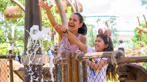 A mother and her young daughter with their hands outstretched over a spurt of water on the Journey of Water, Inspired by Moana trail