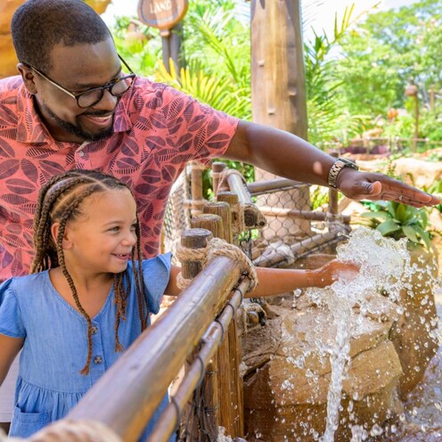 A father and his young daughter with their hands in a water fountain on the Journey of Water, Inspired by Moana trail