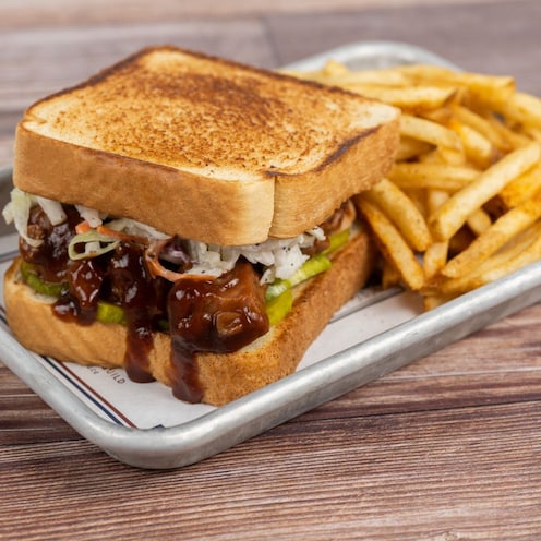 A BBQ Jackfruit Sandwich with coleslaw, pickles and a side of fries