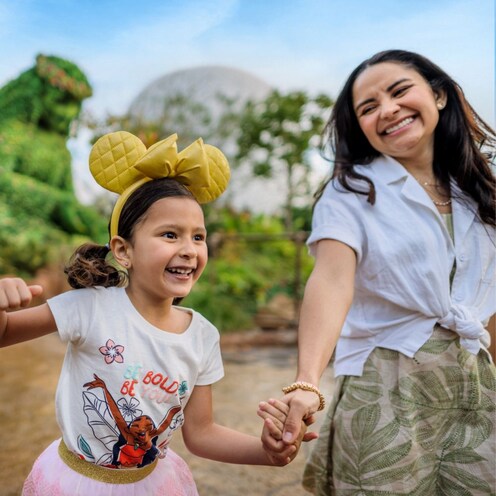 A girl wearing a Minnie Mouse ear headband holding hands with her mother in front of a topiary of Te Fiti