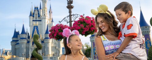 Una madre y sus dos niños pequeños usando artículos de Disney cerca del Cinderella Castle