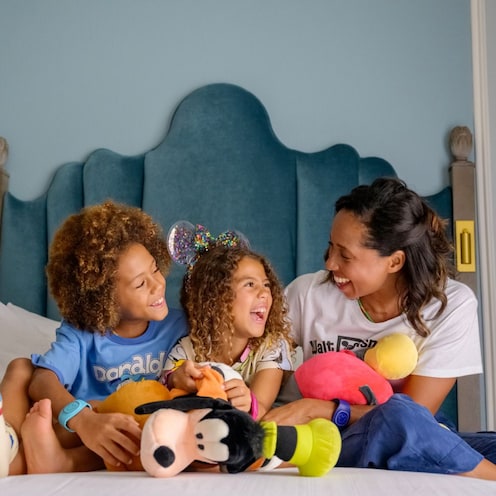 Una madre y dos niños ríen en una cama en una habitación de hotel