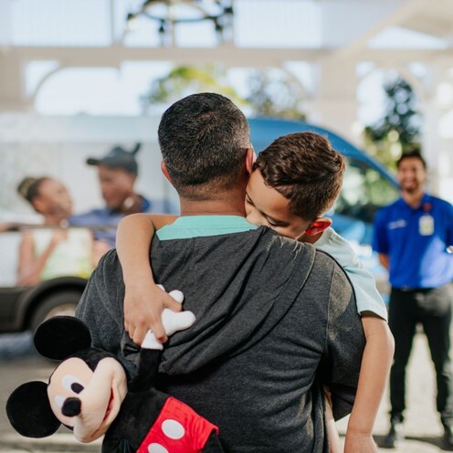 A man holding his son walks toward a van and a driver in an Advent Health uniform