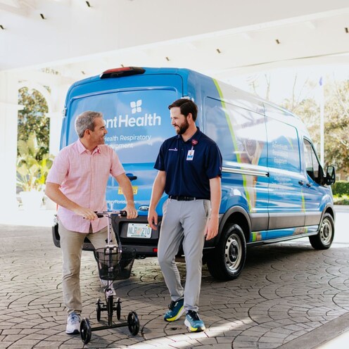 A man in an Advent Health uniform helps another man using a knee scooter 