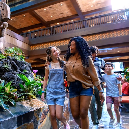 Una familia de 4 personas caminando junto a una escultura Tiki en el atrio del lobby de Disney's Polynesian Village Resort