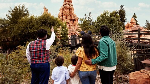 A Cast Member giving a tour to a family of 4, pointing at the peak of Big Thunder Mountain Railroad