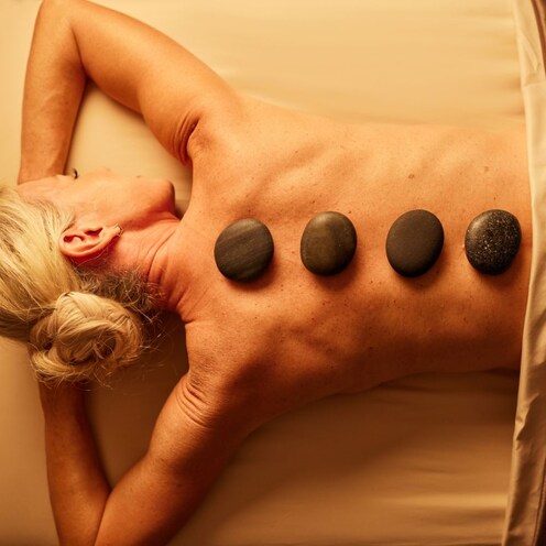 Una mujer disfrutando de un masaje con piedras de río calientes que ayudan a aliviar y relajar el cuerpo.