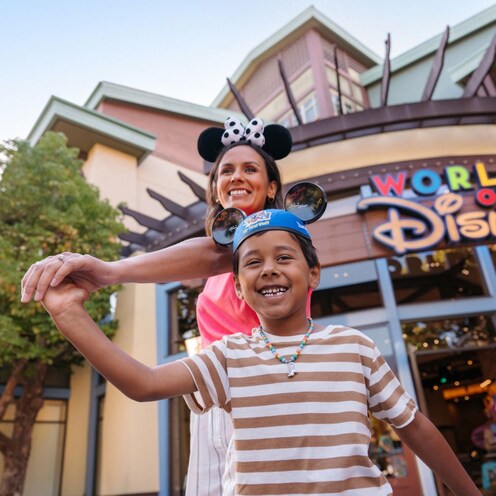 Una mamá y su hijo, tomados de la mano y con gorros de orejas de Mickey Mouse y Minnie Mouse, frente a la tienda World of Disney en Downtown Disney District