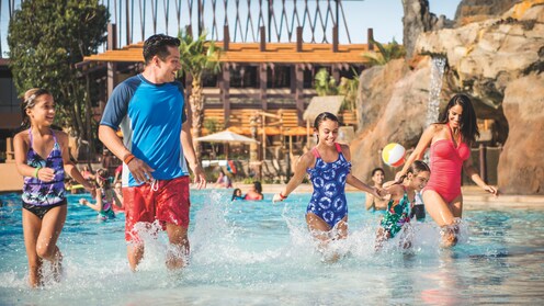 A family of 5 walks near the edge of a beach-style pool at a Disney Resort hotel