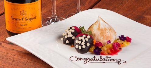 “Congratulations” is written in chocolate on a plate of confections beside a bottle of champagne.