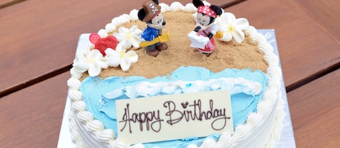A decorated layer cake reading “Happy Birthday” features Mickey and Minnie Mouse in a beach scene