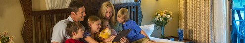 Una familia de 6 en una cama utiliza una tableta digital para planear su día