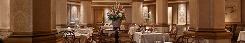 Salão de jantar formal no Victoria & Albert's, com um buquê de flores e mesas postas com porcelanas sofisticadas