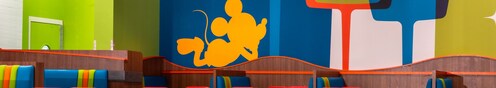 Dining tables and booths with a pop art mural featuring Mickey Mouse at Everything Pop Shopping & Dining in Disney’s Pop Century Resort