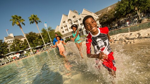 A smiling boy splashes through knee high water with his family watching in the background