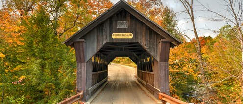 A head-on view of a wooden covered bridge with a sign that reads ‘No Trucks or Buses Allowed’ on a road surrounded by trees