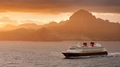 A Disney cruise ship sails past a mountainous shore