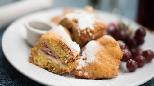 A Battered & Fried Monte Cristo Sandwich with sliced turkey, ham and Swiss cheese served with a side of grapes