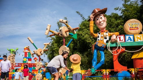 A smiling mom and her child look at the large figure of Woody in Toy Story Land at Walt Disney World Resort