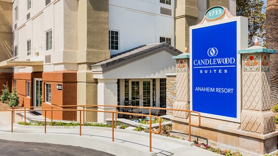The hotel exterior features a wheelchair access ramp, outdoor seating, glass paned doors and a sign that reads 1733, Candlewood Suites, Anaheim Resort