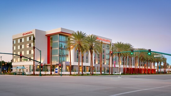 The Hampton Inn & Suites Anaheim Resort Convention Center with large windows and palm trees at the entrance