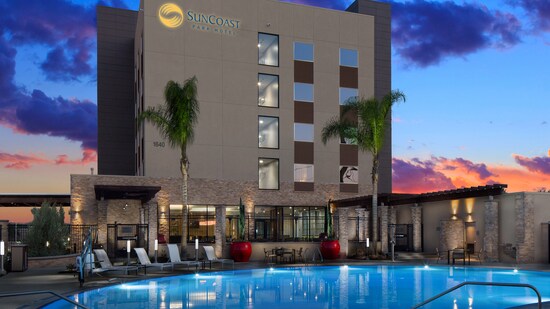 A pool area with tables, chairs, plants and trees outside the SunCoast Park Hotel Anaheim