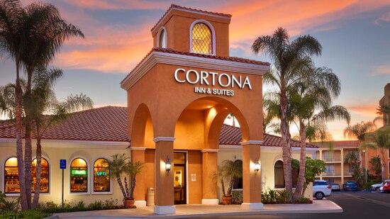 A sunset view of Cortona Inn and Suites Anaheim Resort, featuring an arched entrance, terracotta facade and palm trees