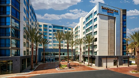 Bedroom has chair and lamp, 2 queen beds with headboards and shared nightstand facing a dresser and wall mounted television