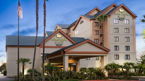 An outside view of Homewood Suites Hilton with landscaping that includes palm trees and an American flag. 