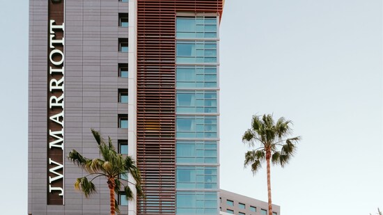 Exterior view of a hotel with windows, 2 palm trees and the words ‘JW Marriott’ on the building facade