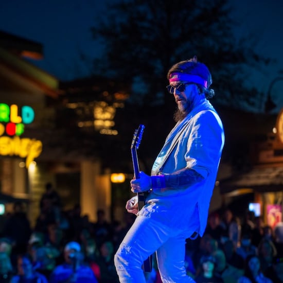 Un hombre tocando una guitarra frente a una multitud cerca de la tienda World of Disney	