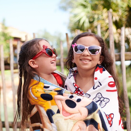 Dos chicas envueltas en toallas de playa, con lentes de sol, abrazadas