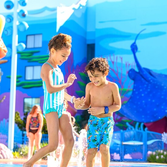 Deux enfants se tenant par la main alors qu’ils s’éclaboussent dans la piscine Flippin’ Fins au Disney’s Art of Animation Resort