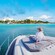 A woman relaxing on the sundeck of a boat while looking out to a tropical beach filled with palm trees and resorts
