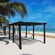 A sandy beach with palm trees and 2 cabanas containing hammocks