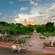 A beautiful park with many trees, with a horse and carriage in the foreground and a stately building in the background