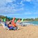 People lounging shoreside on a sandy beach while a lifeguard watches families playing in the water