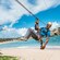 A Guest smiles, riding a zip line that runs over the water at a beach