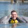 2 dolphins kissing a man on each cheek while he stands in neck deep water