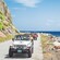People drive 4 Jeep Wranglers on a coastal mountain road near an ocean