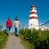 A couple walks along a grassy path toward a lighthouse