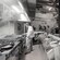 A chef stands in a kitchen in a restaurant full of people