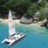 A catamaran sailboat is very close to a shore where a path leads to a resort building