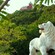 A carved statue of a lion is surrounded by lush trees and a house on a hill